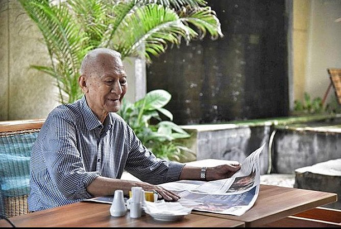 Older man reading a newspaper while relaxing on a terrace